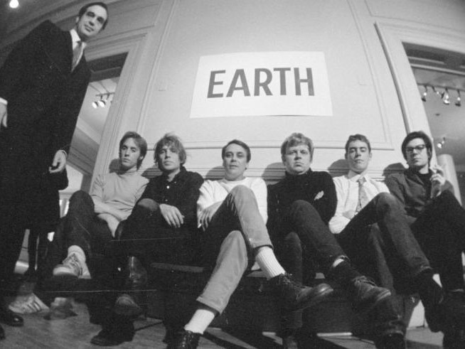 Seven men sitting under an EARTH poster