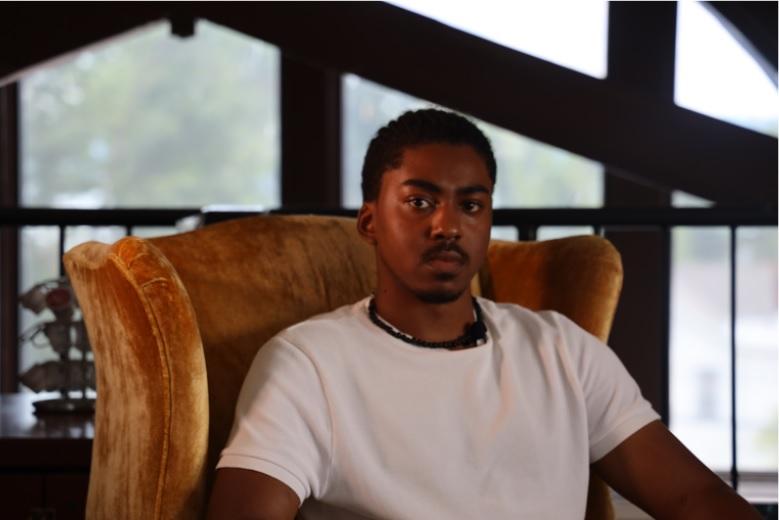 This is an image of Kellen Cooks, who is looking into the camera and is sitting on an armchair.