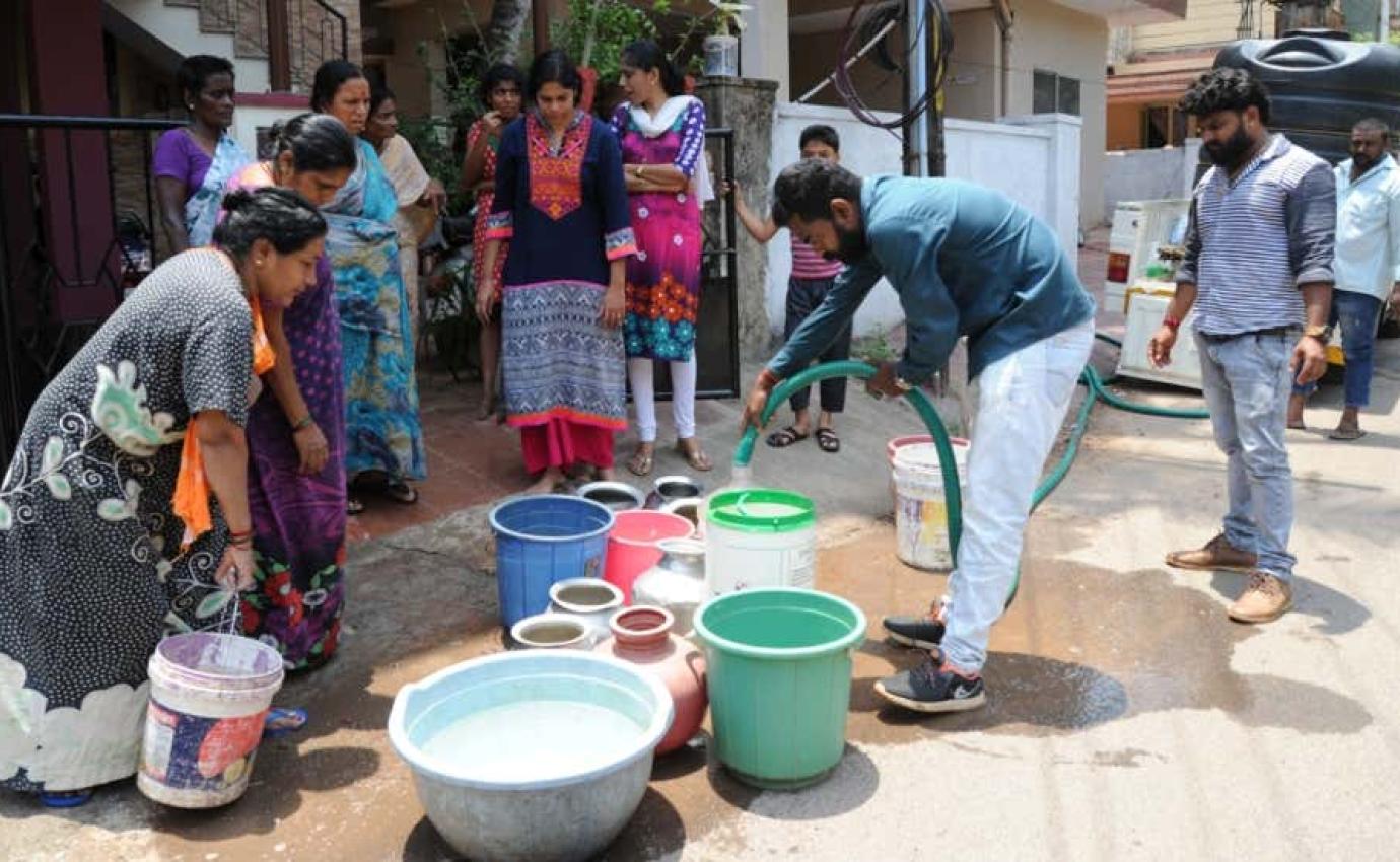 Men and women in India filling water containers with hoses