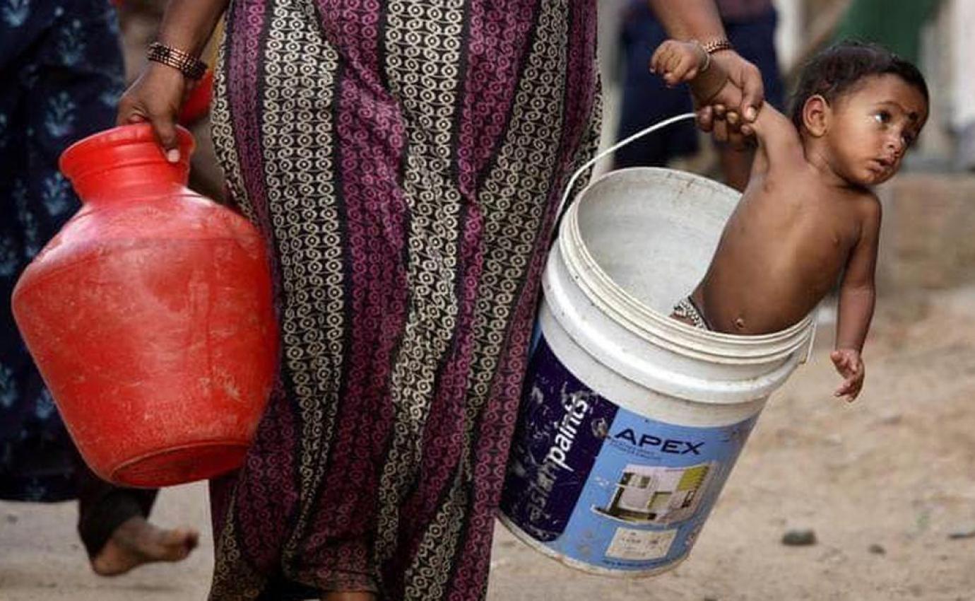 a woman carrying a child and a waterbucket with one hand