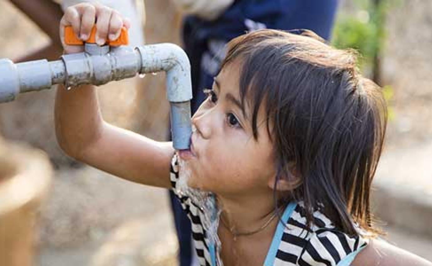 A child drinking water from an outdoor tap